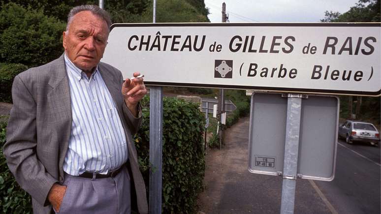 Gilbert Prouteau, autor de uma biografia de Gilles de Rais, em 1992, em frente a uma placa do Castelo do Barba Azul