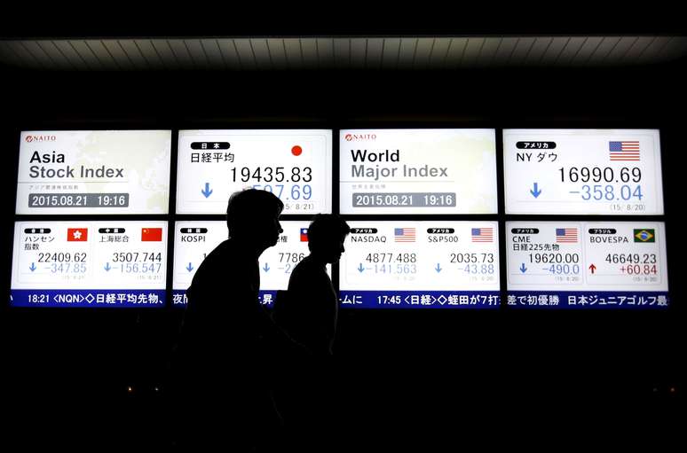 Pessoas caminham em frente a painel com movimentação de mercados 
09/11/2015
 REUTERS/Issei Kato