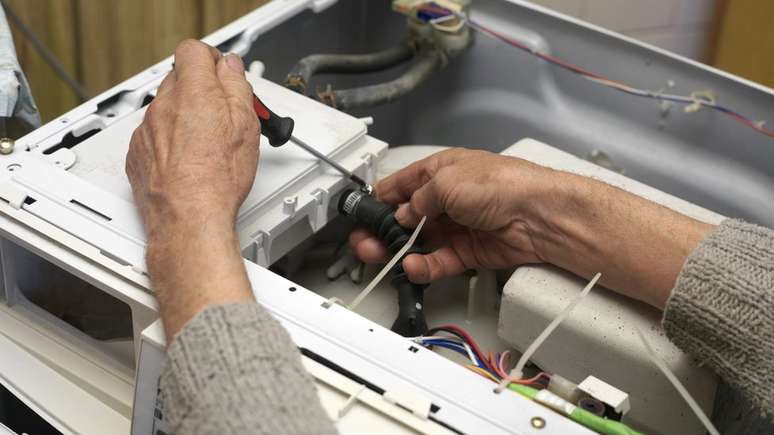 Bra&ccedil;os masculinos reparando um eletrodom&eacute;stico de grande porte