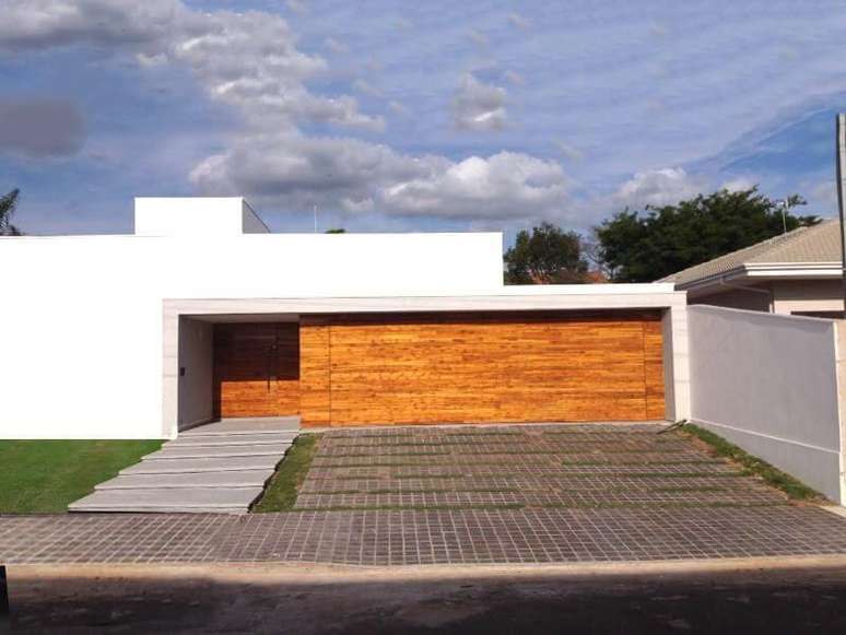 25. Fachada de casa moderna branca com portão de madeira para garagem. Projeto de Hamilton Alme