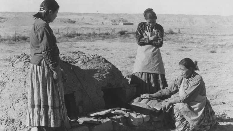 Grupo de mulheres ind&iacute;genas navajo assa p&atilde;o usando um forno de barro: Cultura mede riqueza por quantidade de filhos e n&atilde;o por bens