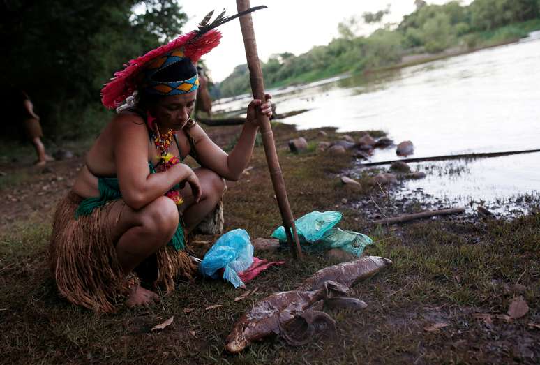 Indígena da tribo Pataxó Hã-hã-Hãe observa peixe morto na margem do rio Paraopeba