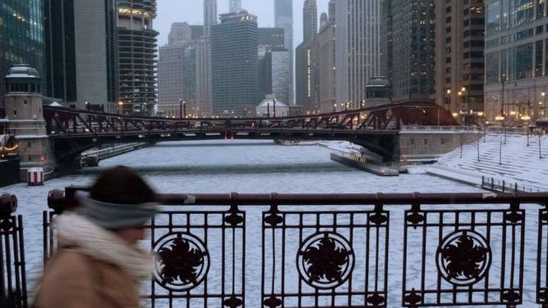 Imagem mostra mulher caminhando em meio a prédios e à área congelada em Chicago, em meio a intensa onda de frio nos EUA