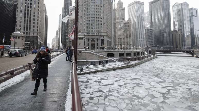Imagem mostra mulher caminhando e outras pessoas na rua em meio a pr&eacute;dios e &agrave; &aacute;rea congelada em Chicago, em meio a intensa onda de frio nos EUA