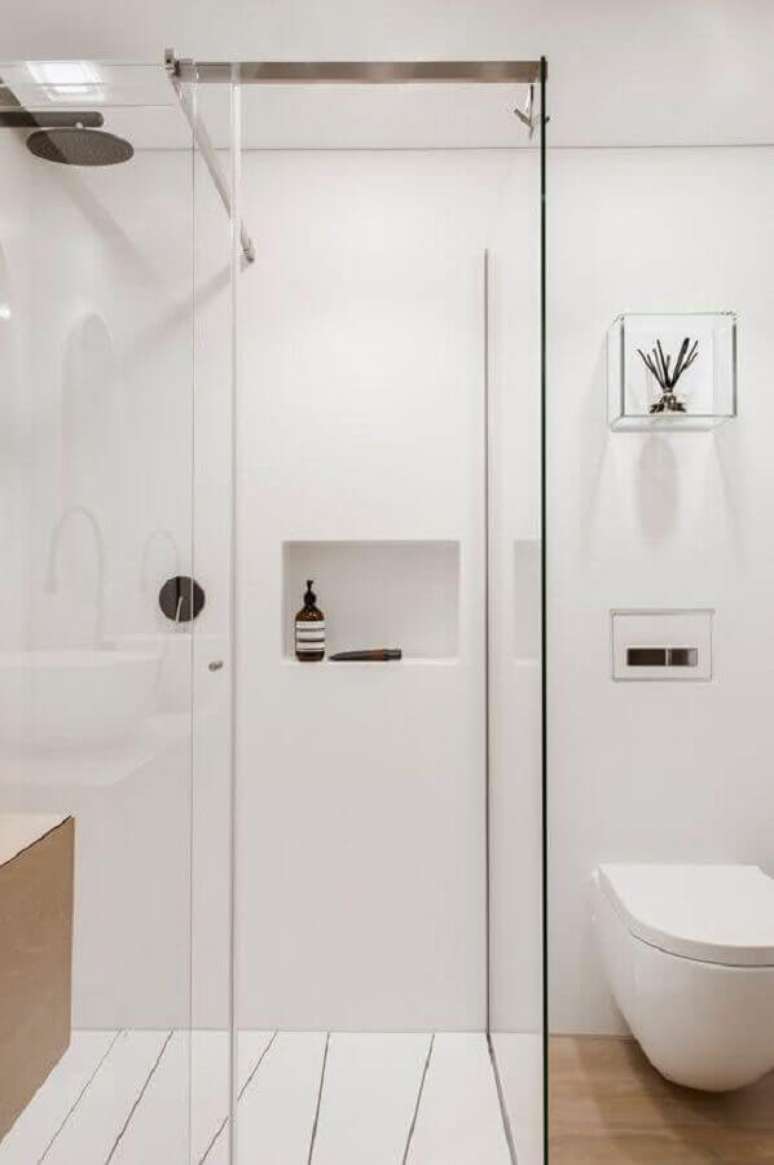 36. Decoração minimalista para banheiro pequeno todo branco com armário e piso de madeira e nicho de vidro – Foto: Hogares Frescos