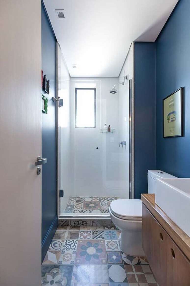 42. Decoração de banheiro pequeno com parede pintada de azul, piso hidráulico e gabinete de madeira – Foto: Pinterest
