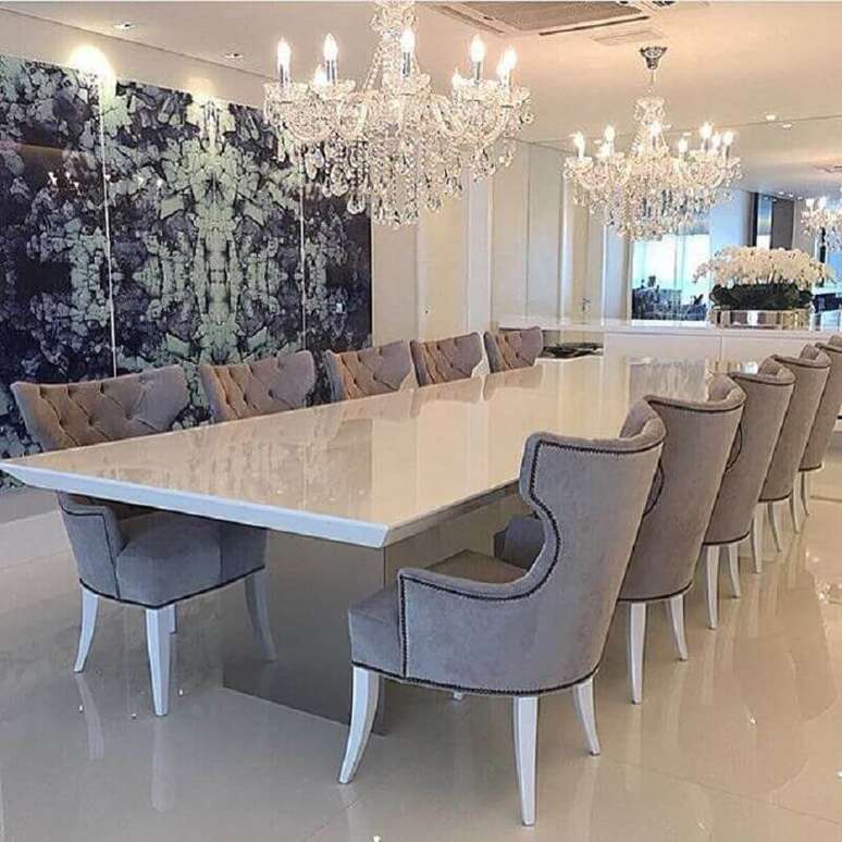 8. Decoração sofisticada em tons claros com dois lustres de cristal para sala de jantar com grande mesa branca e parede espelhada