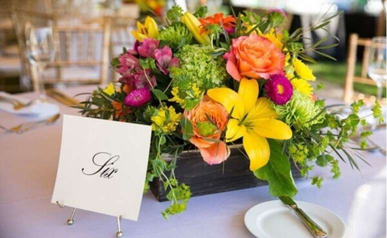 49- O centro de mesa tem caixa de madeira escura com flores do campo coloridas. Fonte: Wedding Wire