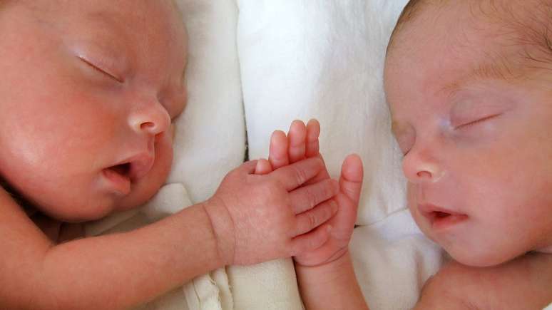 Bebês gêmeos dormindo de mãos dadas