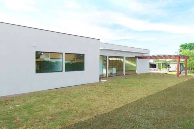 32. Fachada lateral de casa t&eacute;rrea moderna com pergolado de madeira. Projeto de Mateus Castilho