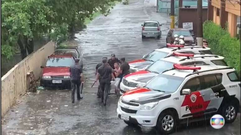 A gravação mostra cinco policiais segurando o homem e o colocando entre viaturas estacionadas