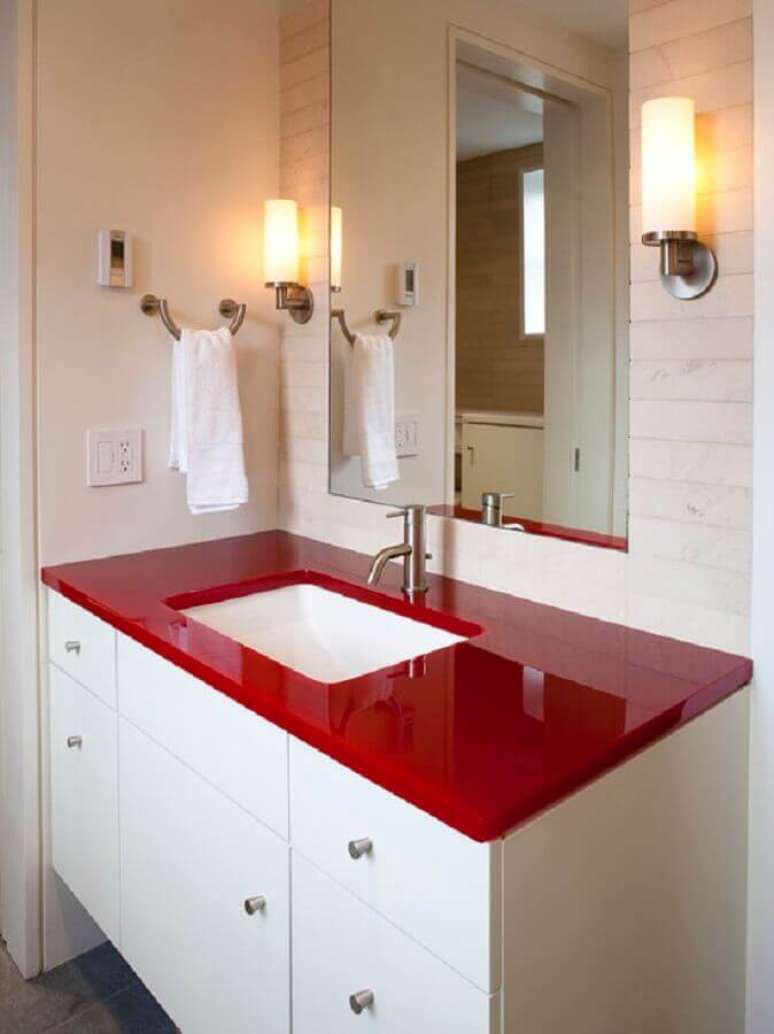 36. Decoração para banheiro branco com bancada vermelha e arandela ao lado do espelho – Foto: Homedit