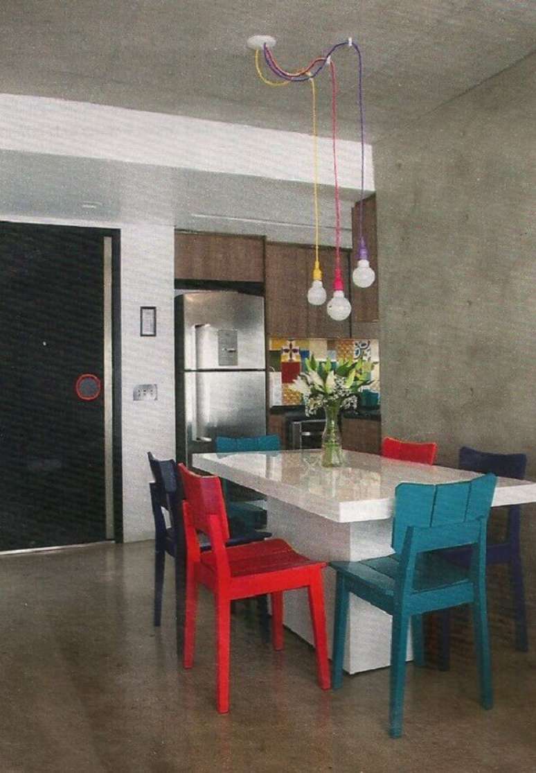 67. Decoração para sala de jantar com cadeiras vermelhas e azuis e pendentes coloridos sobre a mesa branca – Foto: Pinosy