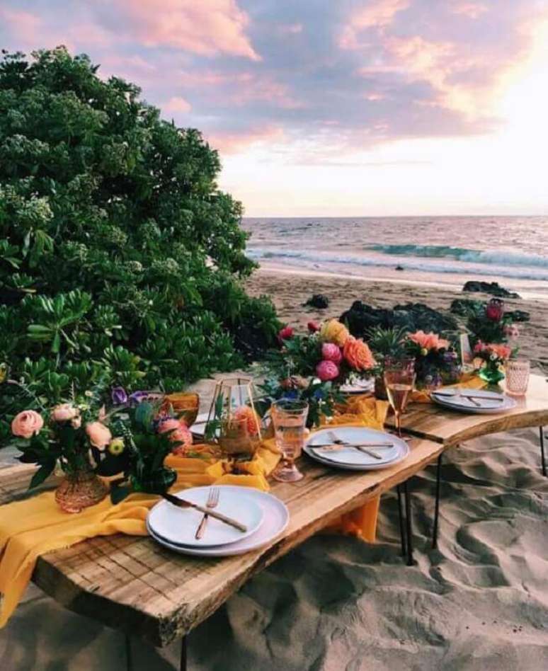 29. Decoração rústica para festa luau na praia com mesa de madeira e arranjos de flores – Foto: Pinosy