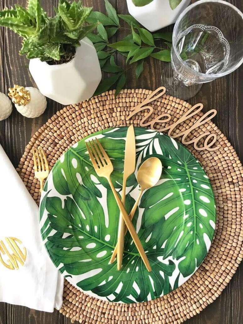 51. Decoração para mesa de festa luau com talheres dourados, sousplat rústico e prato com estampa de folhagens – Foto: Pinterest