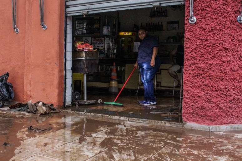 Homem limpa sujeira levada pela enchente no bairro do Cambuci, em São Paulo