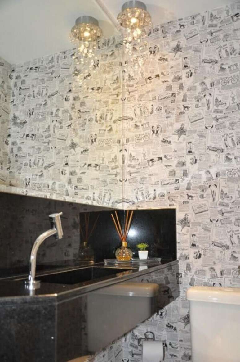 29- O papel de parede para lavabo com padronagem de jornal em branco e preto contrasta com a bancada em mármore na cor preta. Fonte: Serra Vaz Arquitetura