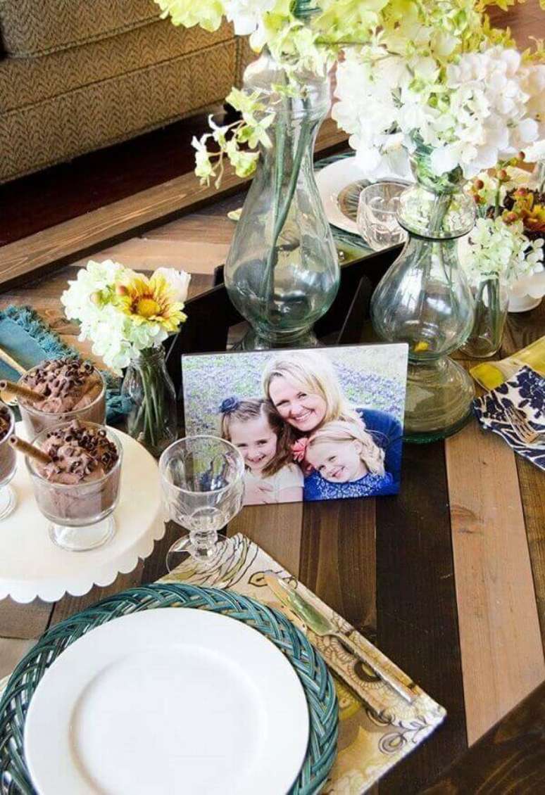 17- A decoração dia das mães tem sobre a mesa arranjos de flores e fotografia da família. Fonte: A Minha Festinha