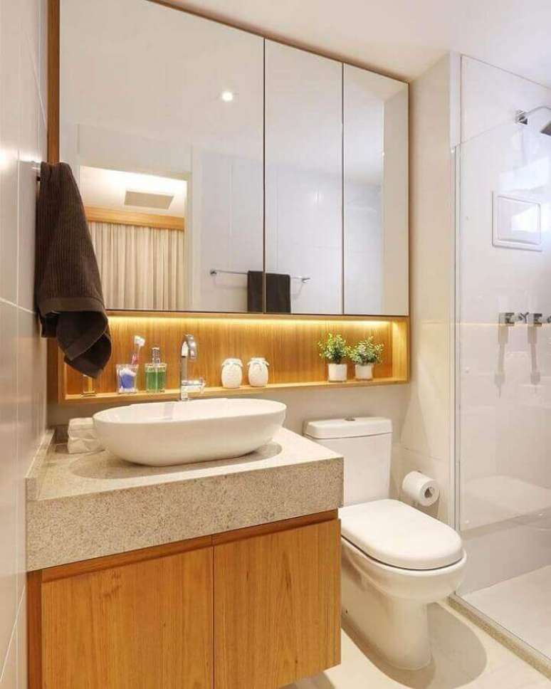 66. Granito branco Siena para banheiro pequeno decorado com armário de madeira com iluminação de LED embutida – Foto: Sesso & Dalanezi