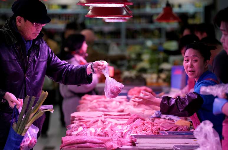 Um comprador recebe carne de porco de um vendedor em um mercado em Pequim. REUTERS/Jason Lee