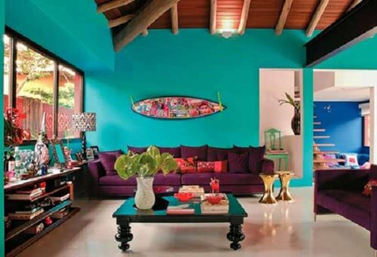 31 – A parede da sala de estar com tinta azul turquesa combinou com os elementos decorativos nas cores pink e roxo presentes no ambiente. Fonte: Casa Casada