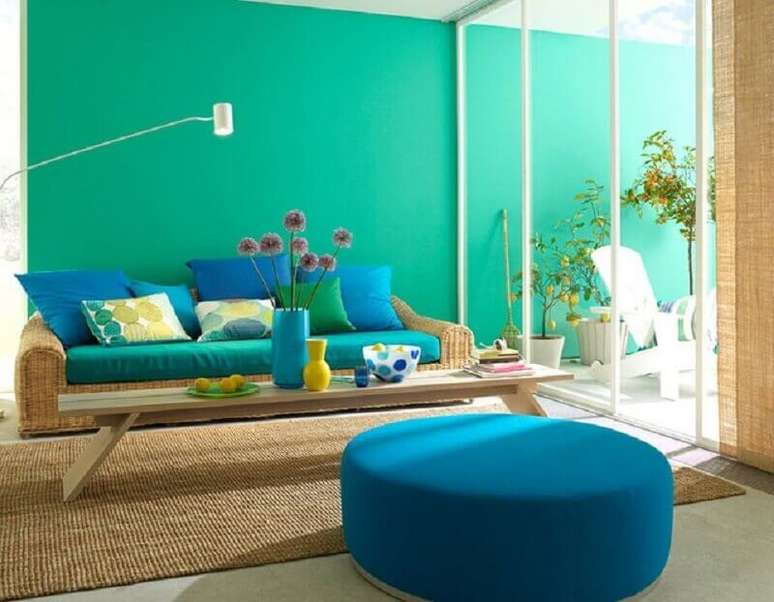 21. Decoração com parede verde água para sala com sofá de vime e puff redondo azul – Foto: Jaeger Arquitetura