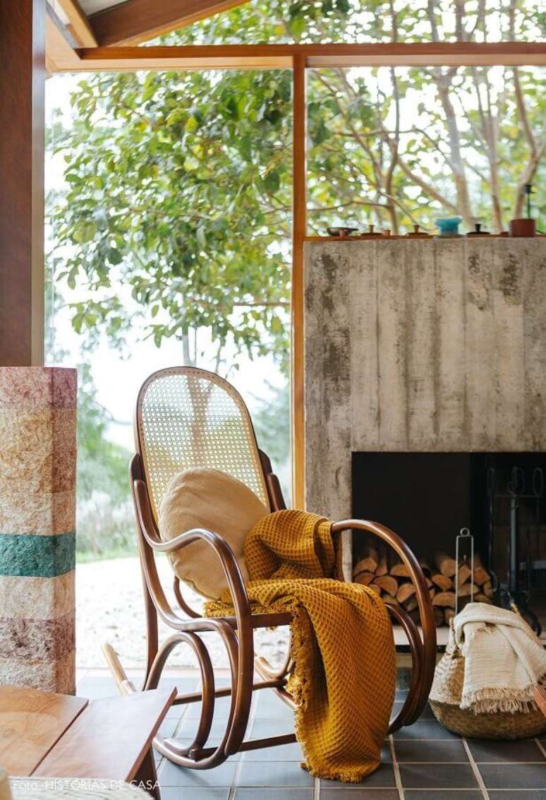 37. Decoração rústica com cadeira de balanço de madeira e lareira – Foto: Histórias de Casa