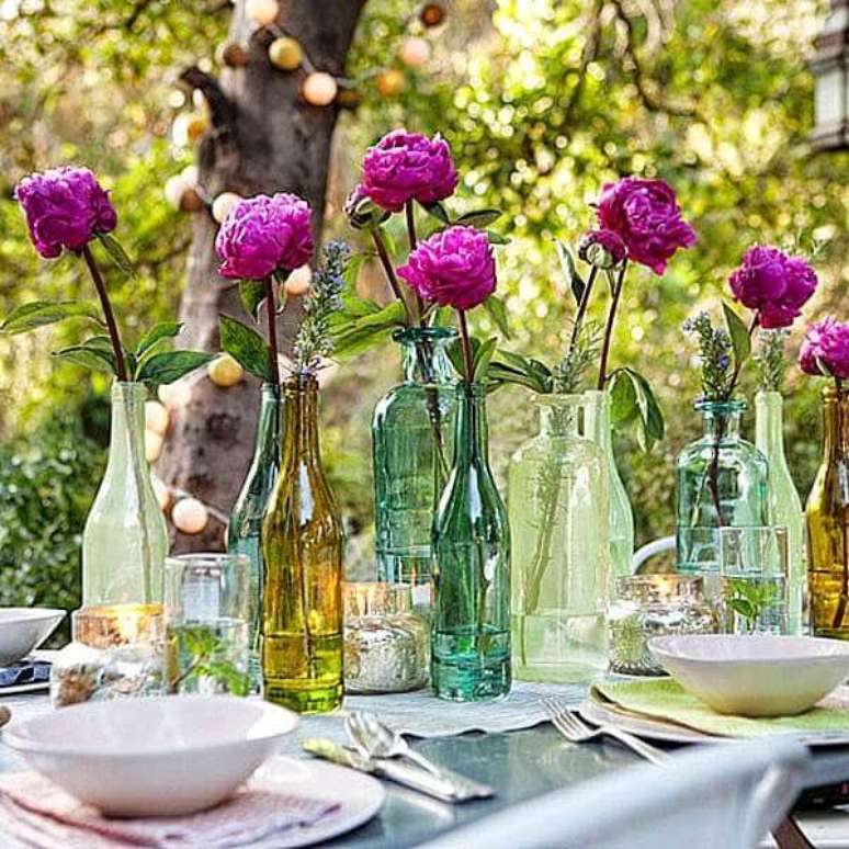 18- A decoração dia das mães em ambiente aberto tem garrafas coloridas em diferentes formatos com flores no centro da mesa. Fonte: Casa para Viver