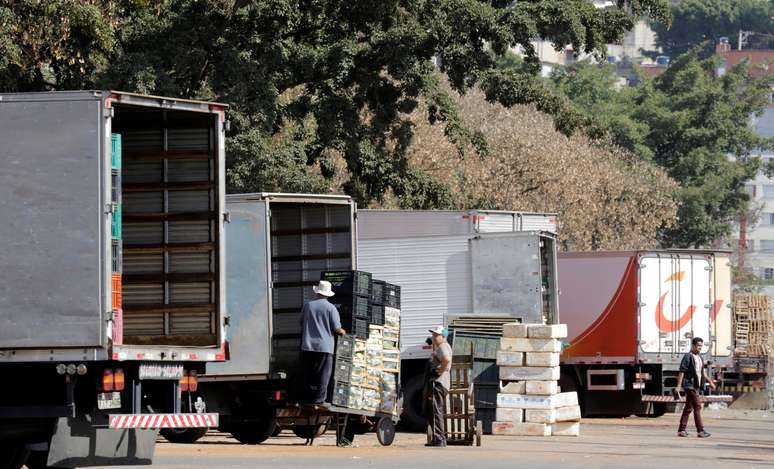 Funcionário descarregam caixas com vegetais de caminhões em São Paulo