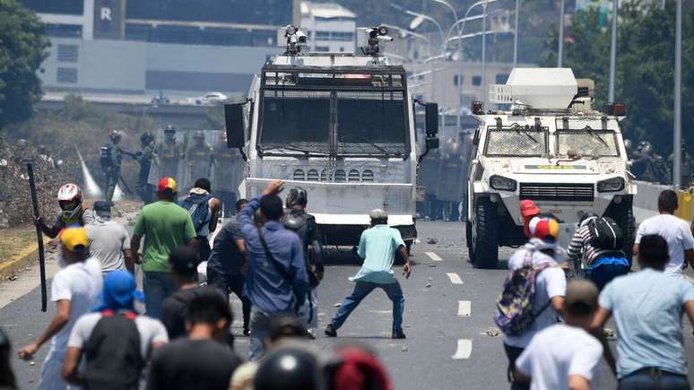 Manifestantes venezuelanos atiram pedras contra veículos em frente a base do Exército