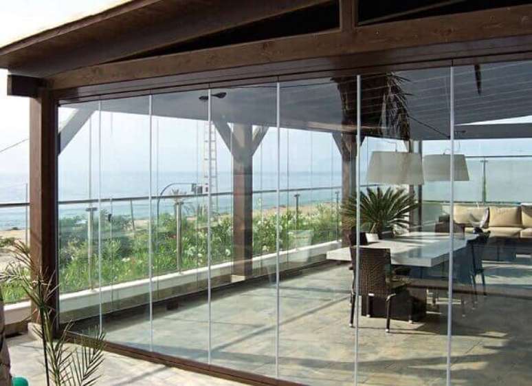 54- A cortina de vidro quando instalada em cobertura rústica no jardim, cria um espaço protegido, bonito e aconchegante. Fonte: PS do Vidro
