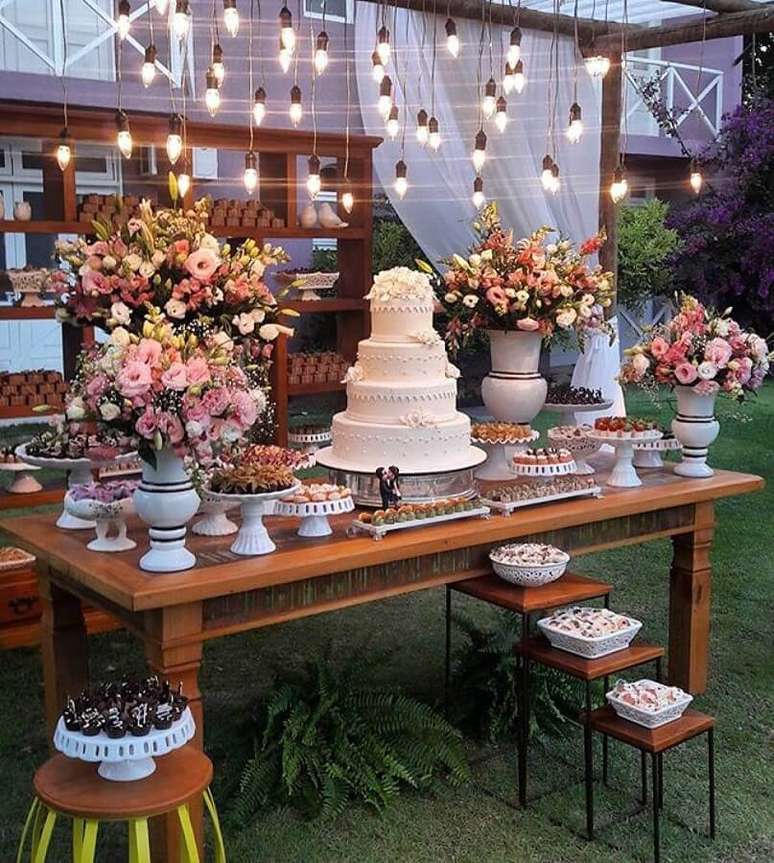35. Linda mesa de festa de casamento ao ar livre decorada com lumárias pendentes e arranjo de flores – Foto: Doce Sabor – Buffet e Recepção