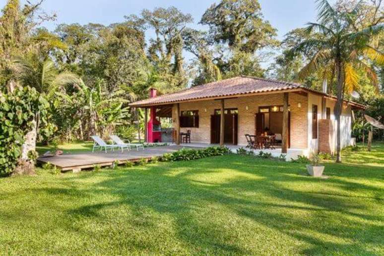 7- A casa de campo r&uacute;stica com tijolo aparente tem paisagismo exuberante ao redor. Fonte: RAC Arquitetura