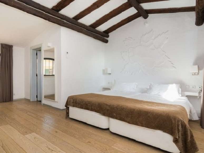 18- A casa rústica tem detalhes de toras de madeira no teto do quarto de casal. Fonte: Engel & Völkers