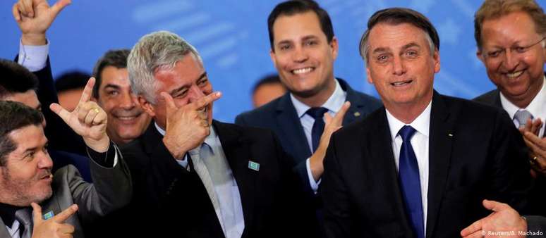 Bolsonaro durante a cerimônia de assinatura do decreto, cercado por aliados que fizeram gestos imitando armas com as mãos