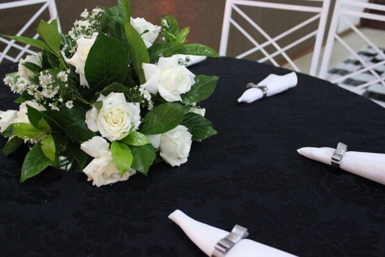 50- Na decoração bodas de prata, as mesas têm toalhas pretas, arranjo de flores e guardanapos brancos com laços prata. Fonte: Buffet cortello