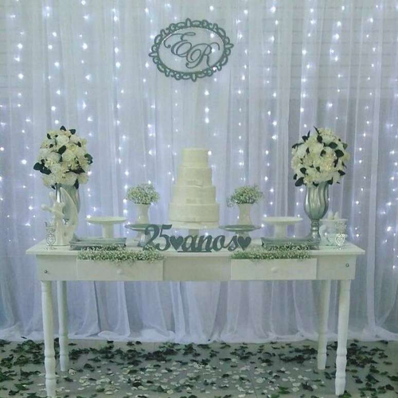 52- O bolo bodas de prata foi colocado sobre um aparador branco decorado com flores no mesmo tom. Fonte: Ateliê das Gêmeas