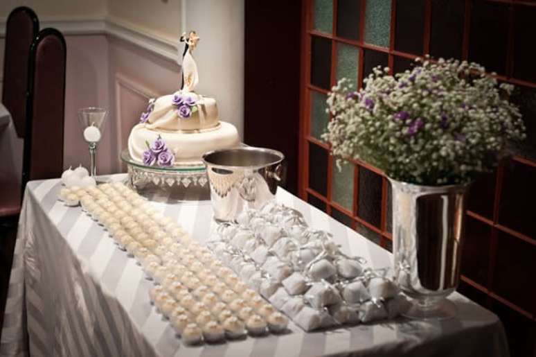 19- A festa de bodas de prata simples tem mesa com bolos, docinhos e lembrancinhas na cor branca. Fonte: Segredos da Vovó