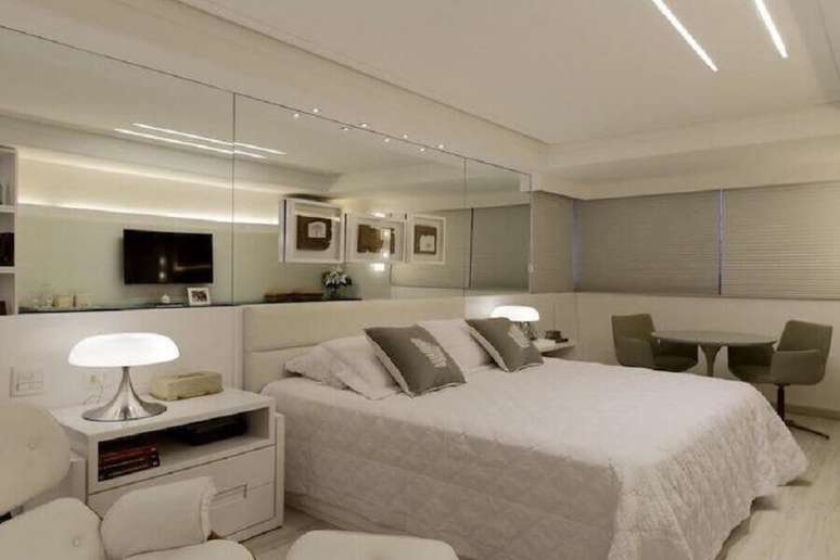 2. Decoração moderna com abajur para quarto de casal amplo todo branco com parede espelhada – Foto: Ana Cunha Arquitetura