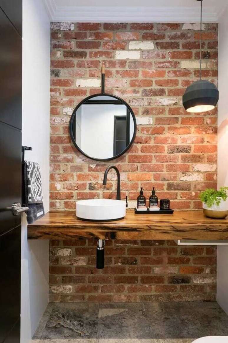 35. Decoração rústica com espelho redondo para banheiro com parede de tijolinho e bancada de madeira – Foto: MdeMulher