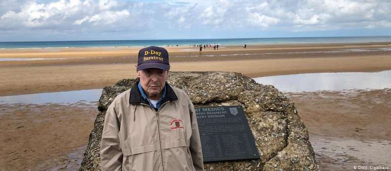 Veterano da Segunda Guerra americano Ray Lambert diante da placa em sua homenagem, na praia de Omaha
