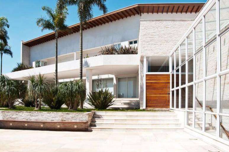 7. Casa linda com uma fachada moderna que usa vários revestimentos, criando uma composição com o paisagismo. Projeto por Crisa Santos