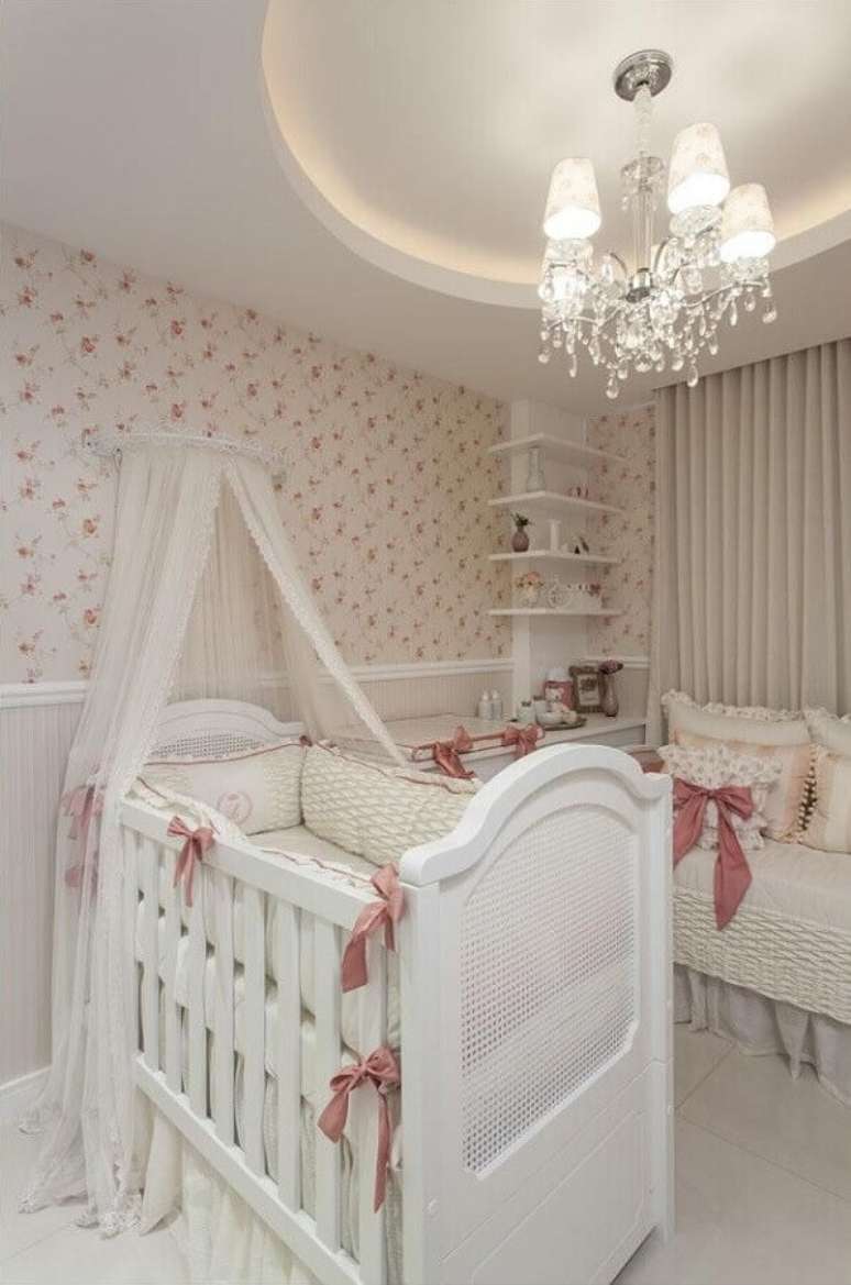 35. Quarto de bebê menina decorado com papel de parede florido e lustre clássico