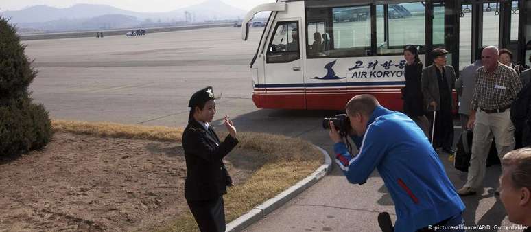 Turista europeu fotografa uma funcionária norte-coreana do aeroporto de Pyongyang, após chegar num voo vindo da China