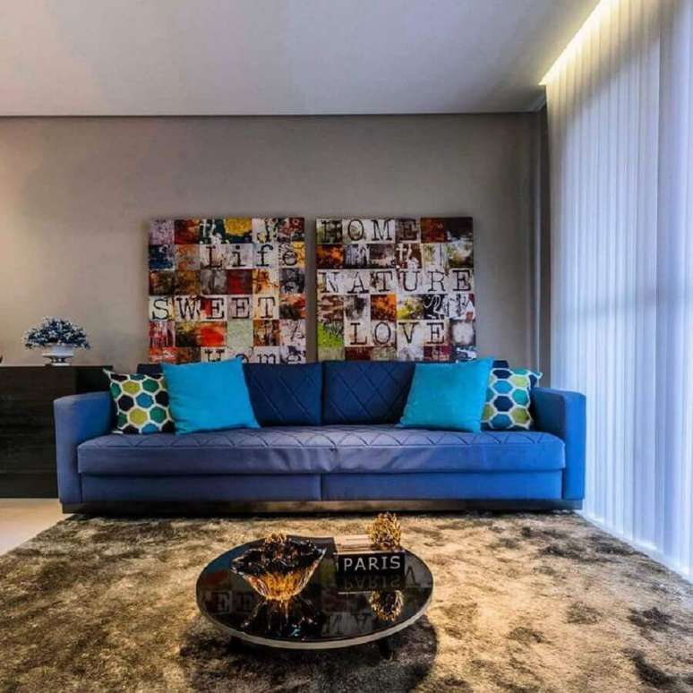 26. Decoração para sala com sofá azul e quadros grandes coloridos – Foto: Lo Interiores
