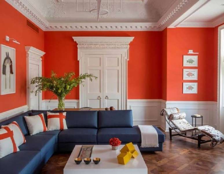 58. A sala com sofá de canto azul também pode receber paredes com cores vibrantes como a cor laranja – Foto: Jean de Just