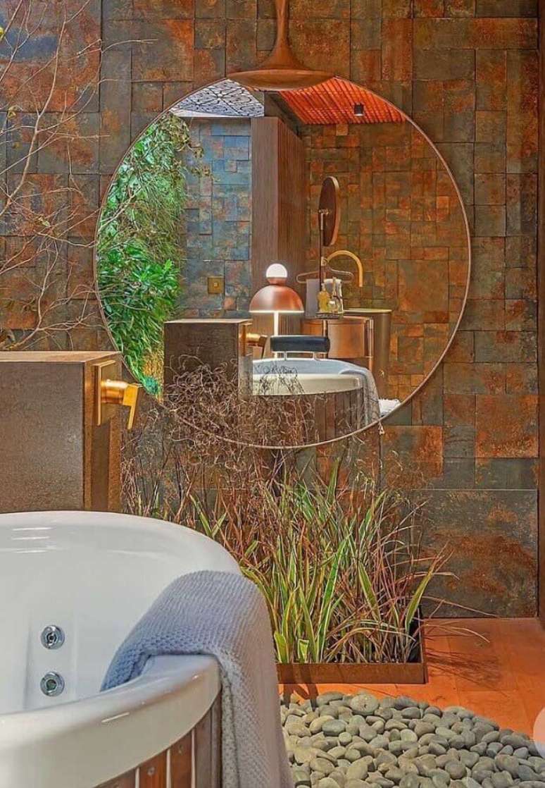 21. Decoração para banheiro com banheira, espelho redondo e revestimento pedra ferro – Foto: Mister Cryl Tintas