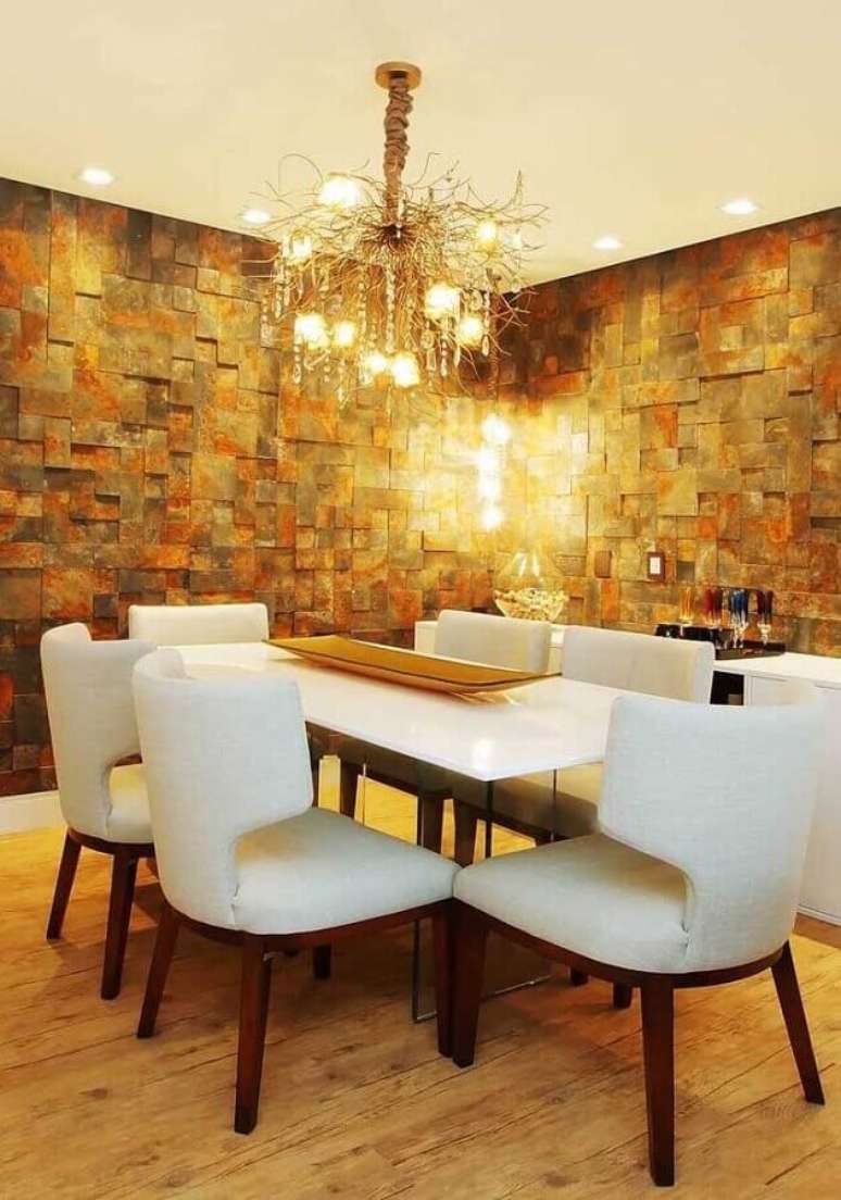 22. Decoração para sala de jantar com cadeiras brancas, lustre arrojado e parede com revestimento pedra ferro – Foto: Pinterest
