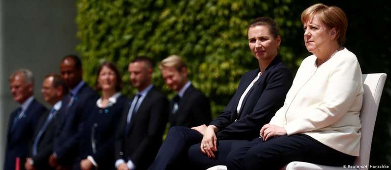 Merkel (dir.) e Frederiksen escutam sentadas os hinos nacionais durante cerimônia em Berlim