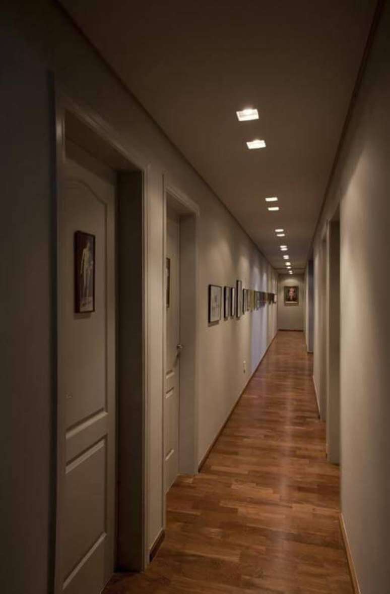 19. Corredor longo com piso de madeira e iluminação embutida. Projeto de AMC Arquitetura
